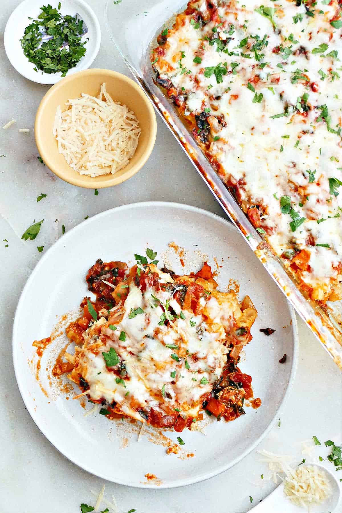a serving of baked ziti on a plate next to a baking dish and toppings