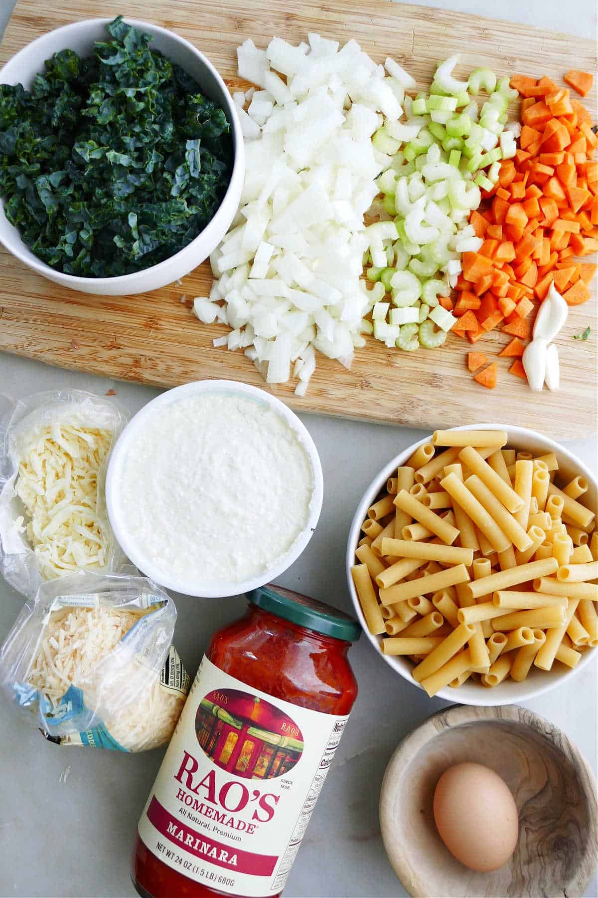 chopped kale, onion, celery, carrot, and garlic next to other baked ziti ingredients