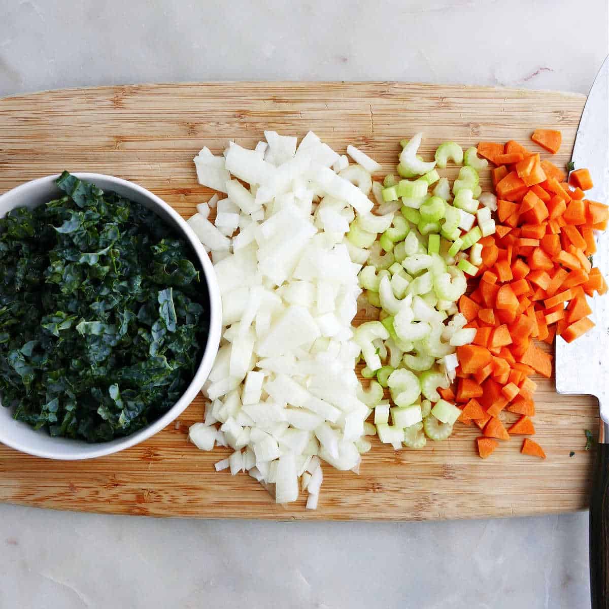 chopped kale, onions, celery, and carrots on a cutting board