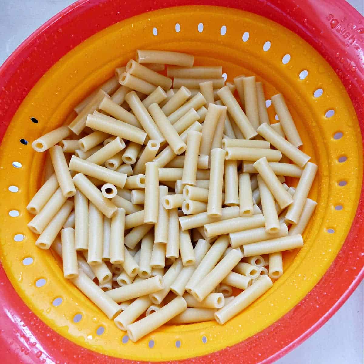boiled ziti being drained in a colander in the sink