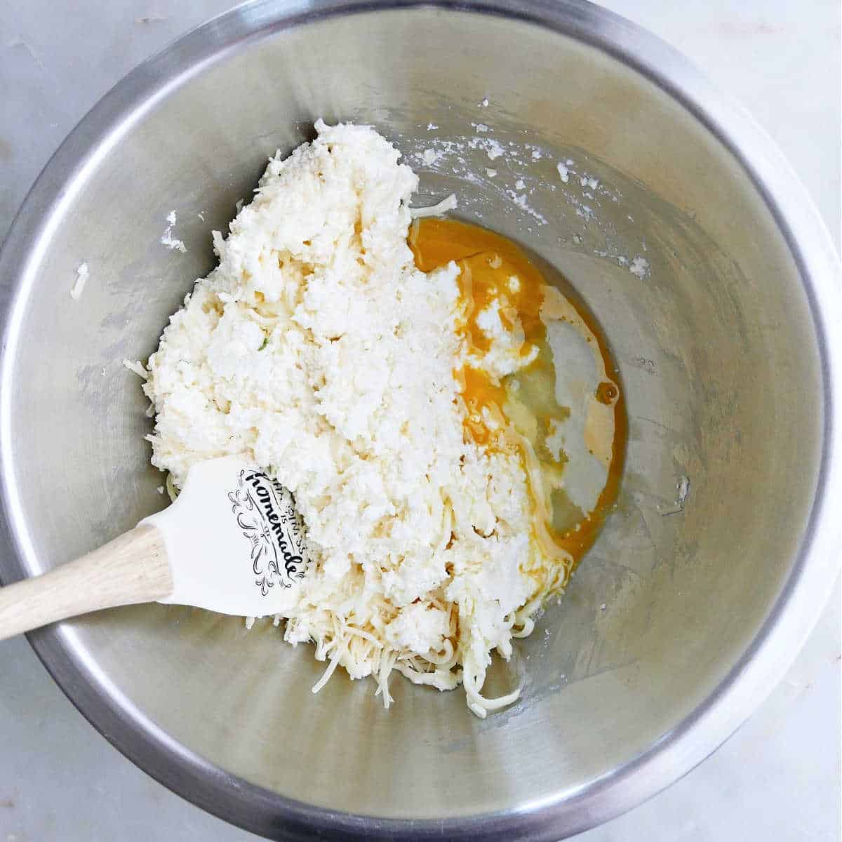 mozzarella, parmesan, and ricotta cheeses being mixed with a beaten egg in a bowl