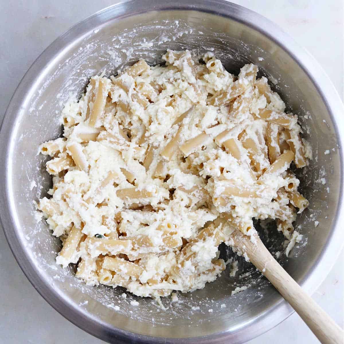 boiled ziti being mixed with mozzarella and ricotta cheese in a bowl