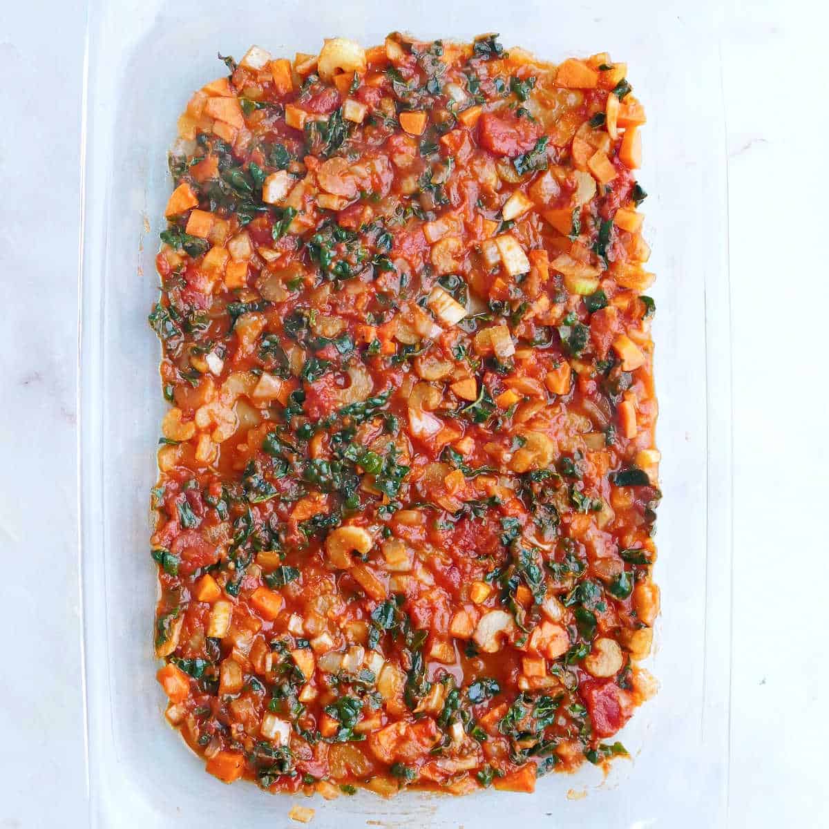 vegetable tomato sauce spread in the bottom of a glass baking dish
