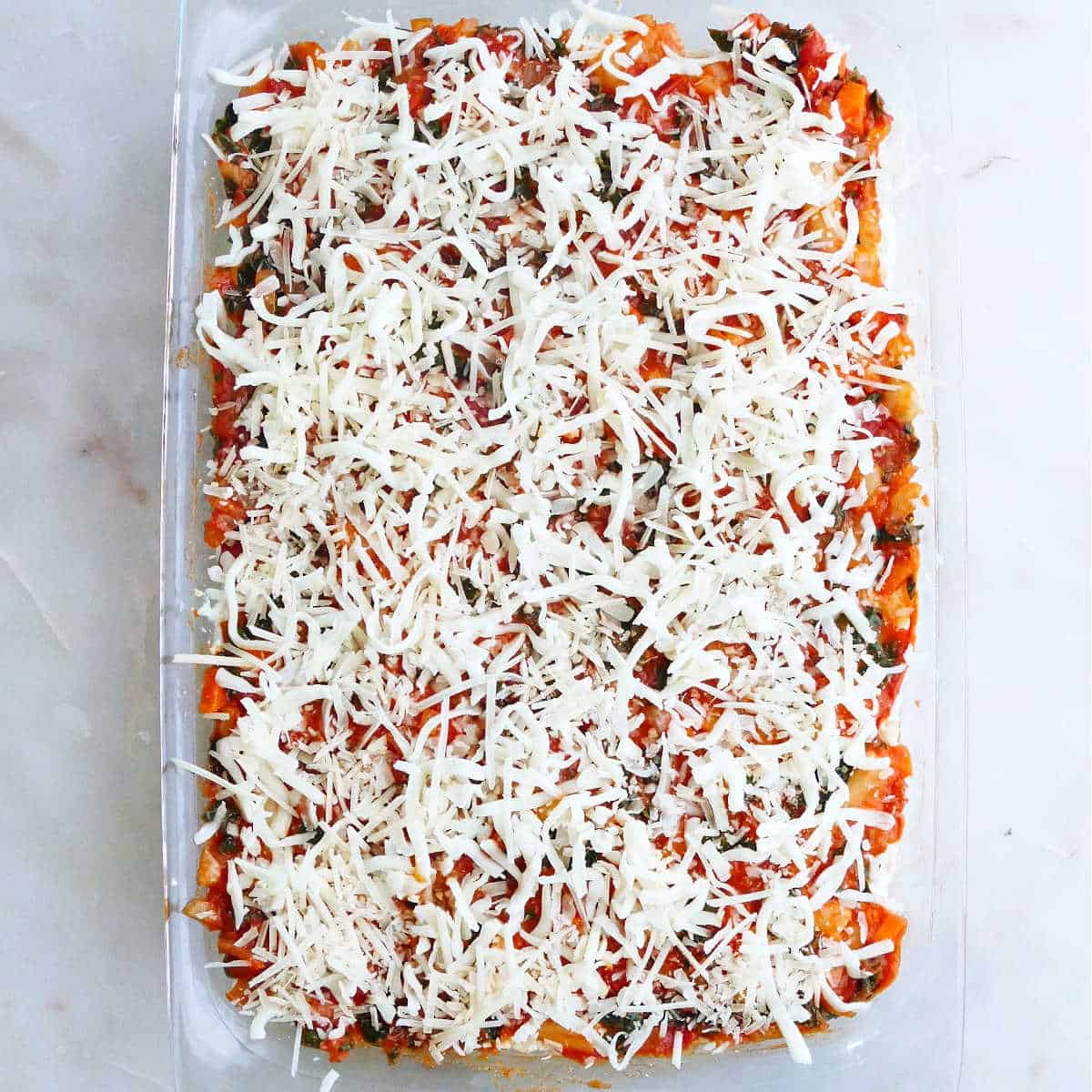 baked ziti topped with shredded cheese before going into the oven