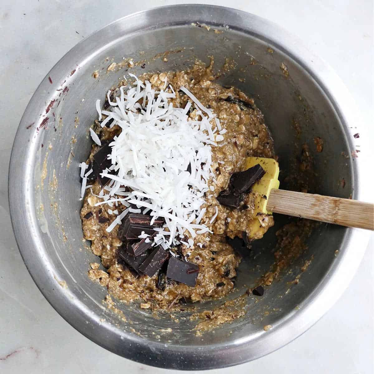 coconut and chocolate being added to cookie batter in a mixing bowl