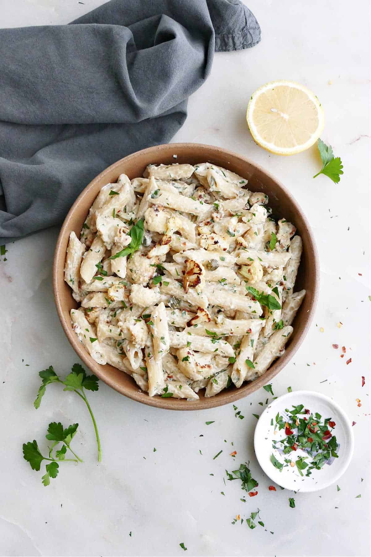 tahini pasta in a serving bowl next to herbs, lemon, and a napkin