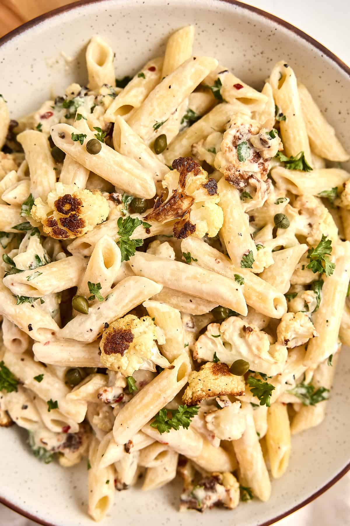 Pasta with tahini sauce, roasted cauliflower, capers, and parsley in a bowl.