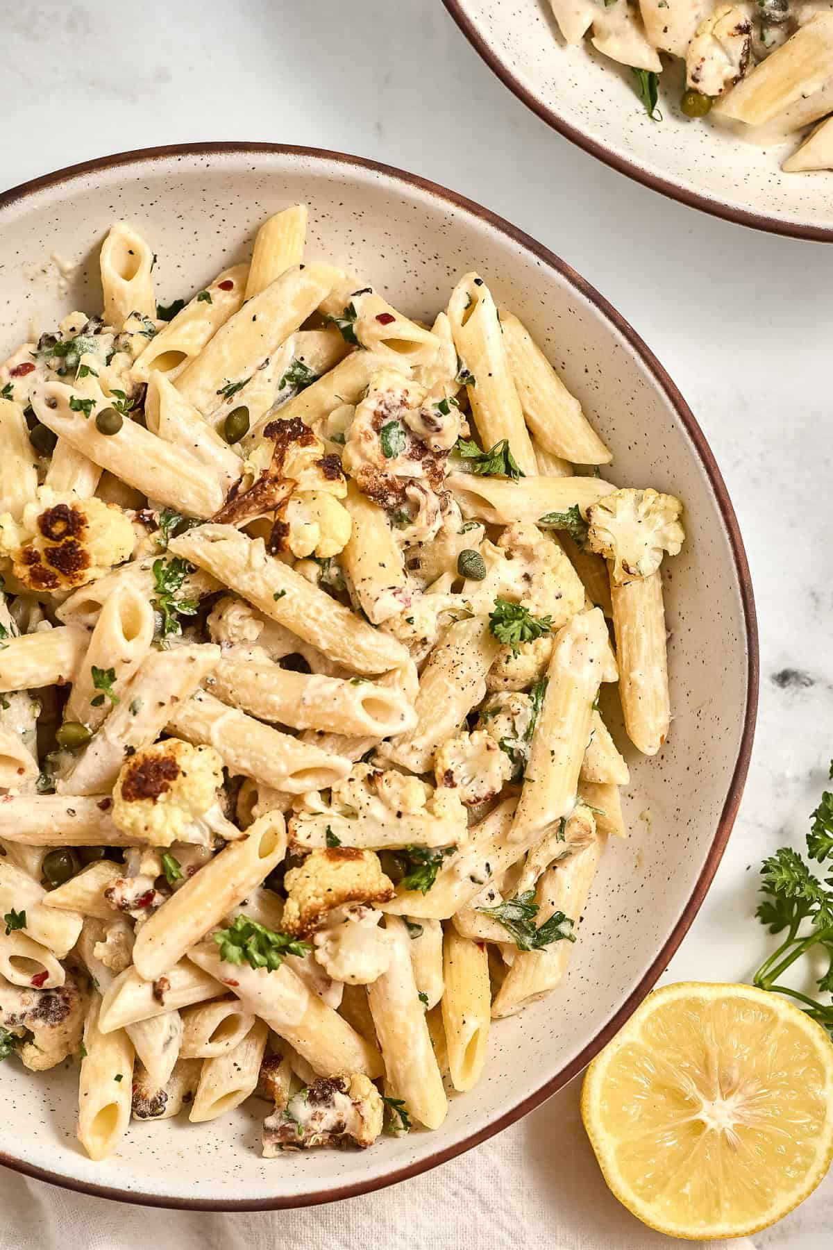 Tahini pasta with cauliflower and capers in a bowl next to lemon and parsley.