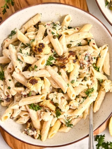 Cauliflower tahini pasta in a bowl on a board next to ingredients.