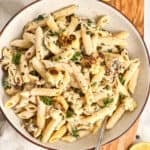Tahini pasta in a bowl on a board next to lemons, parsley, and a napkin.