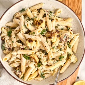 Tahini pasta in a bowl on a board next to lemons, parsley, and a napkin.