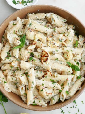 tahini pasta with cauliflower in a bowl next to herbs and lemon
