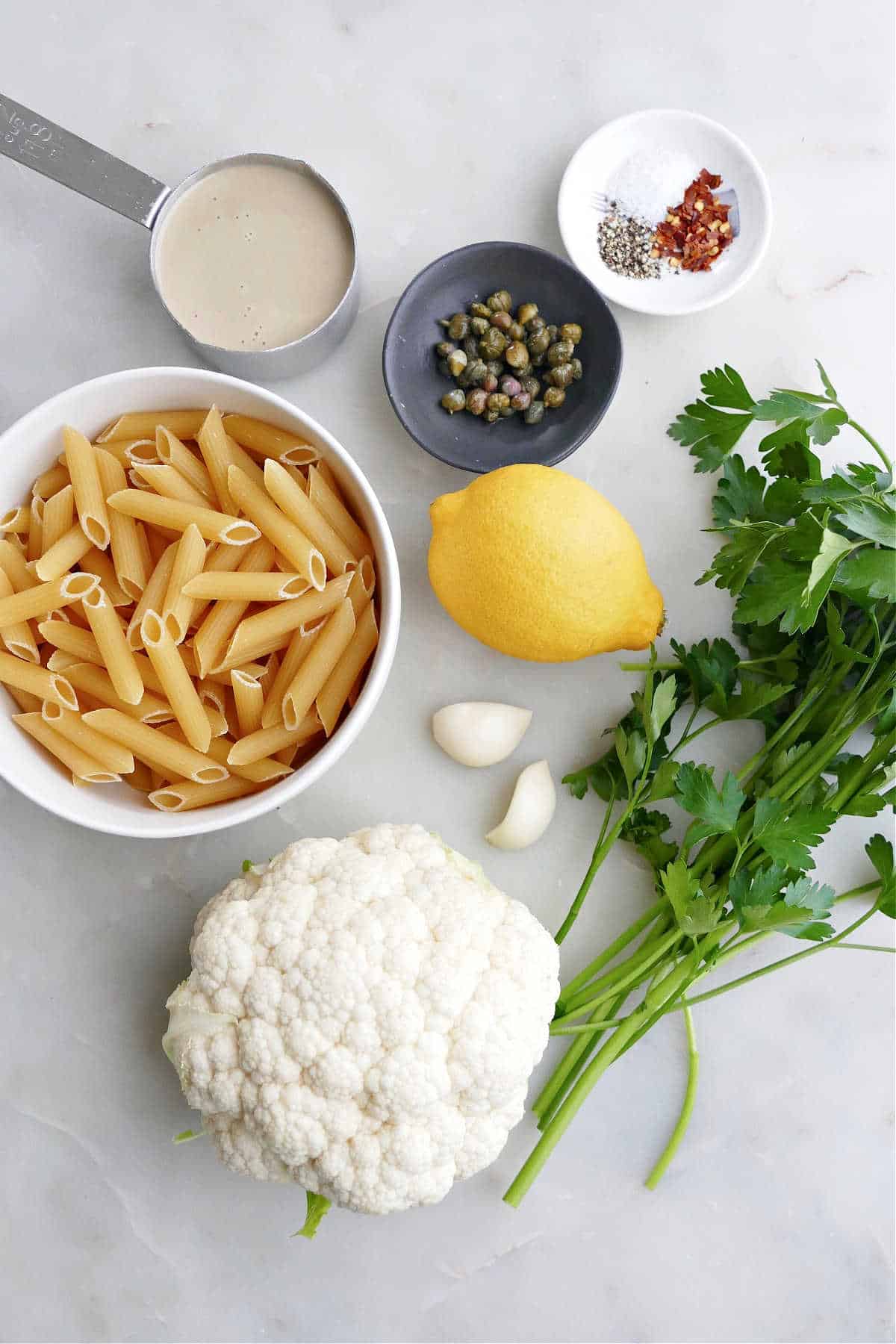 tahini, capers, spices, lemon, parsley, garlic, cauliflower, and pasta on a counter