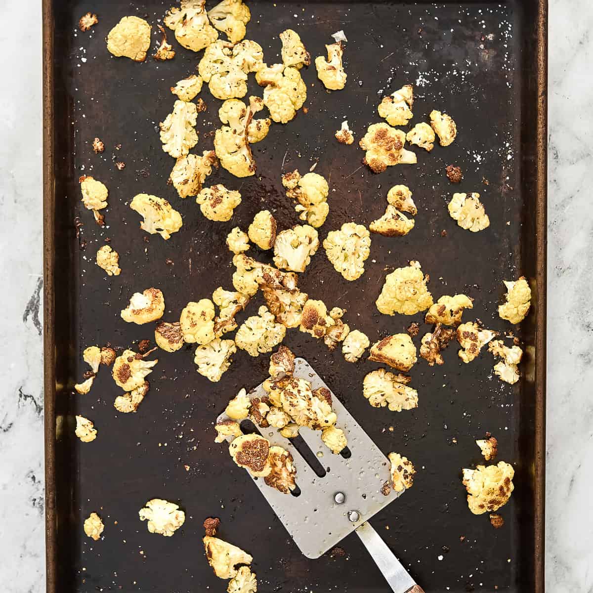 Cauliflower florets on a baking sheet with a spatula after being roasted.