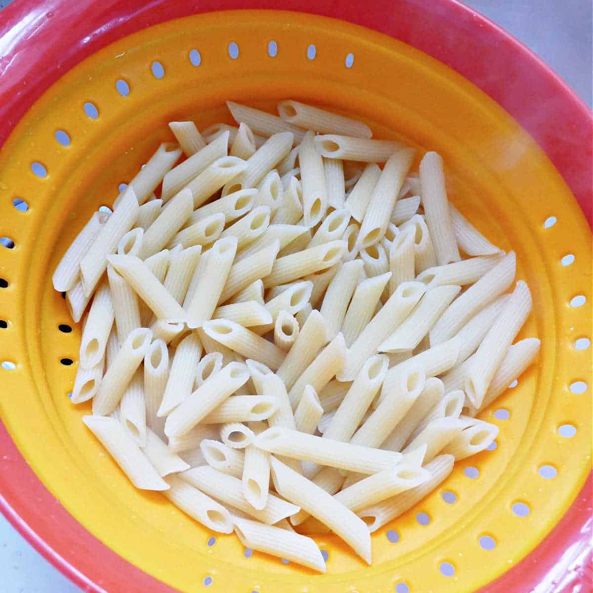 cooked penne pasta in a colander being drained in the sink