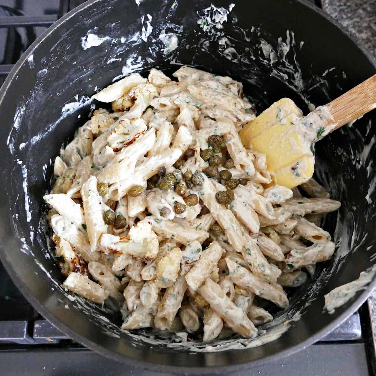 tahini pasta being mixed with cauliflower and capers in a pot