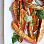 sweet potato wedges drizzled with a green tahini sauce on a tray