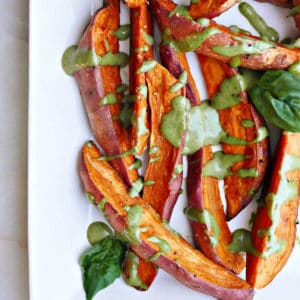sweet potato wedges drizzled with a green tahini sauce on a tray