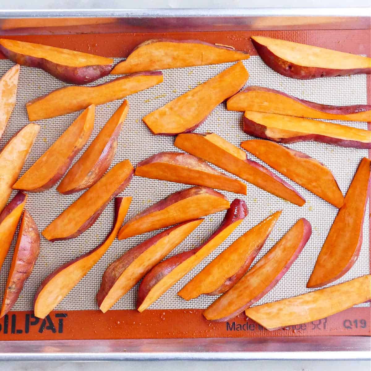 sliced sweet potato wedges on a baking sheet before being roasted