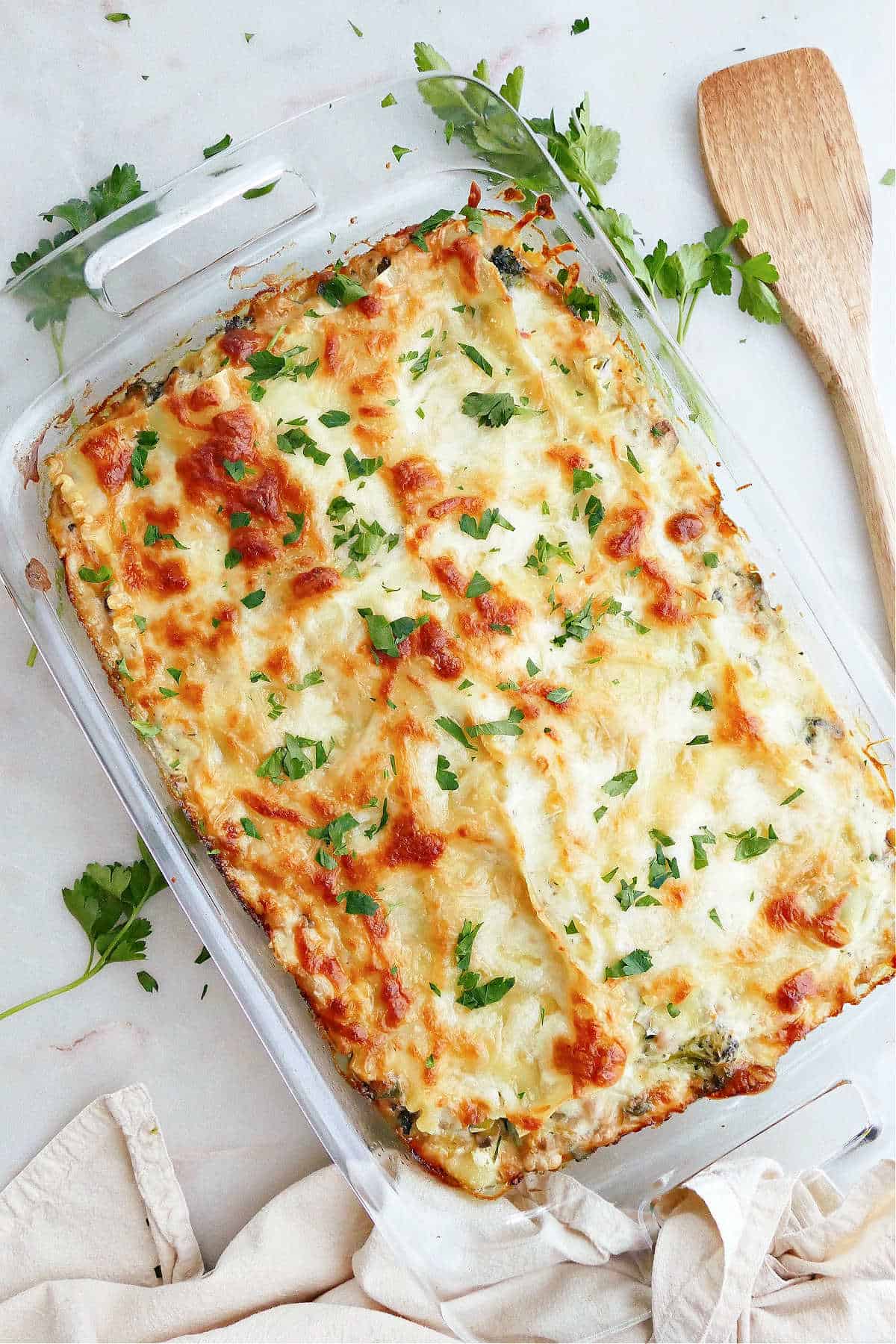 white lasagna in a baking dish topped with parsley on a counter