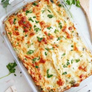 white lasagna in a baking dish topped with parsley on a counter