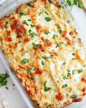 white lasagna in a baking dish topped with parsley on a counter