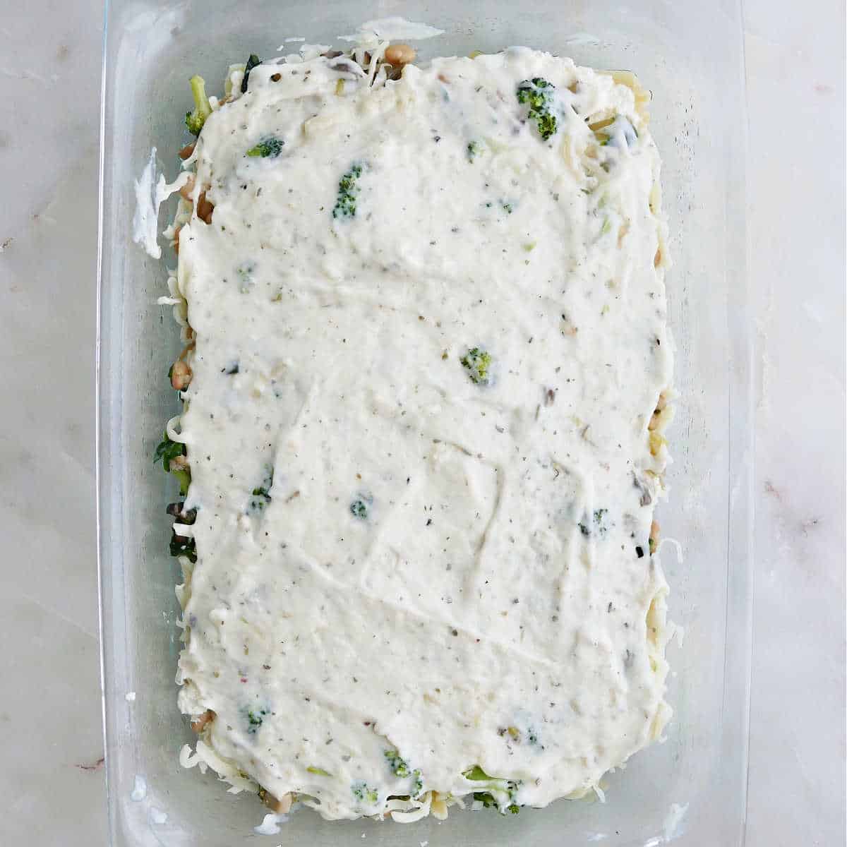 lasagna ingredients topped with white sauce in a baking dish