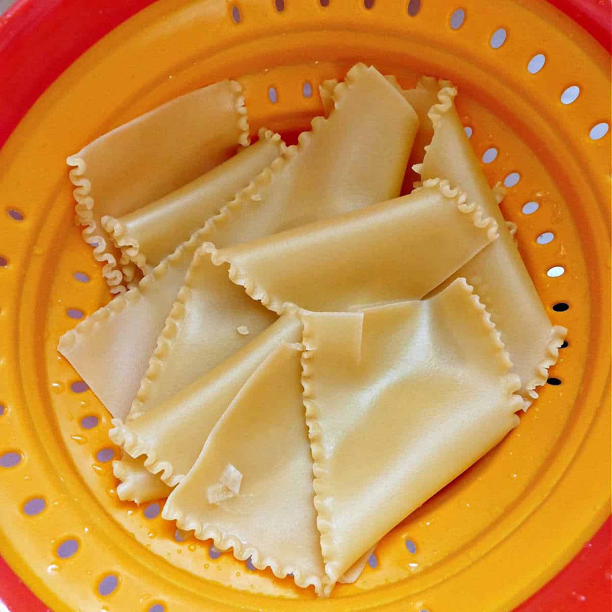 boiled lasagna noodles draining in a colander over the sink