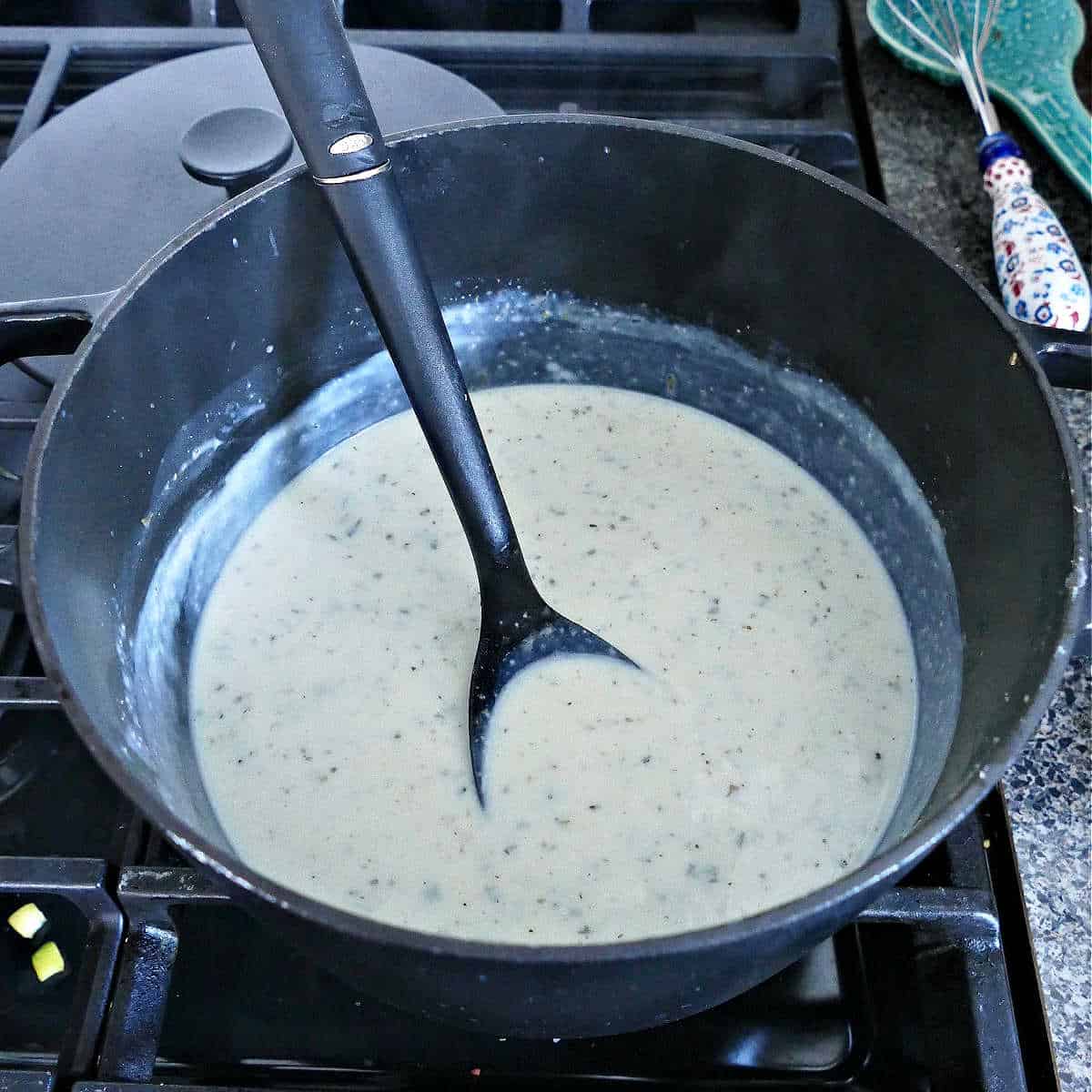 white béchamel sauce cooking in a pot with a spoon inside