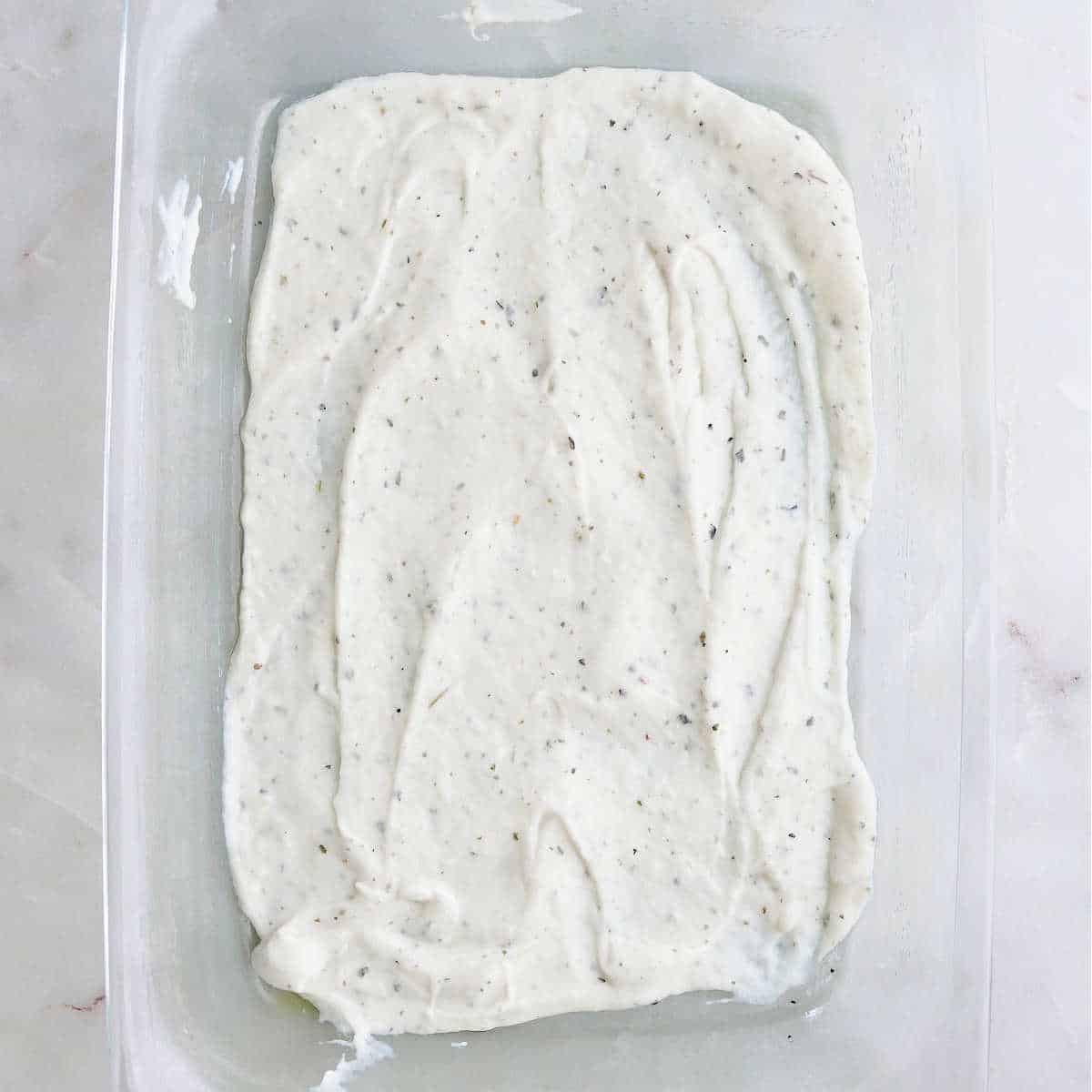 white sauce spread on the bottom of a glass baking dish