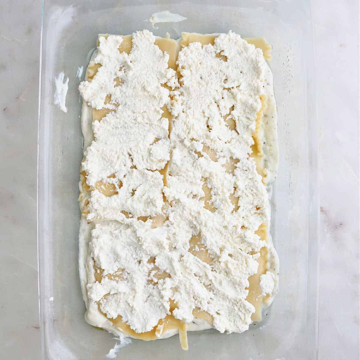 white sauce, lasagna noodles, and ricotta cheese in a glass baking dish