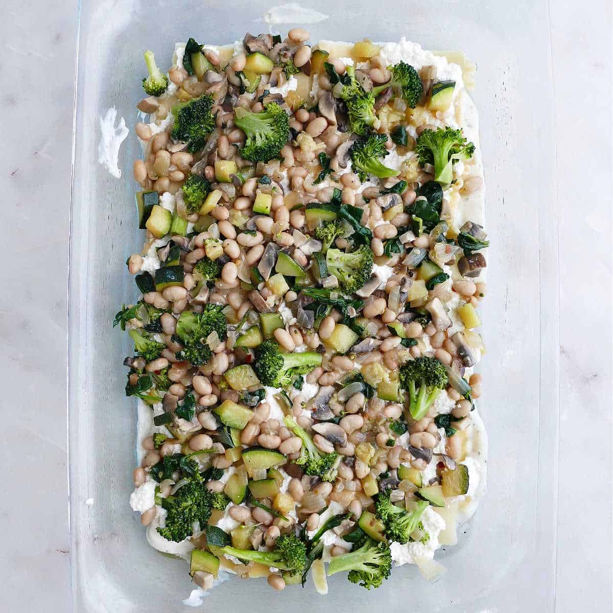 cooked vegetables on top of ricotta, lasagna, noodles, and sauce in a baking dish