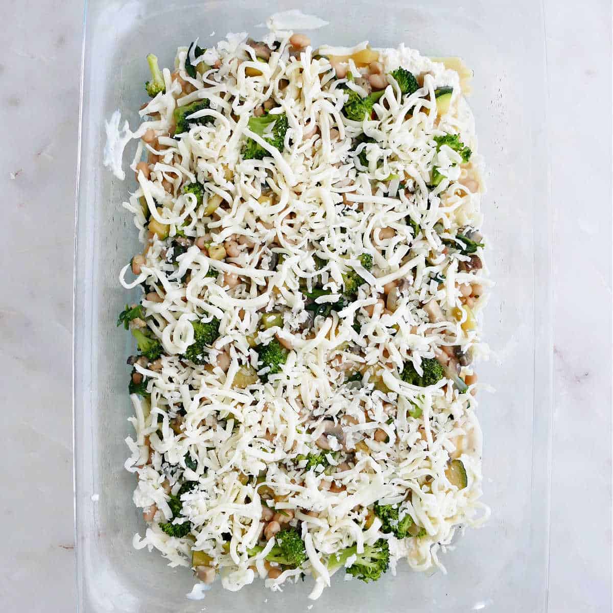 lasagna ingredients topped with shredded cheese in a baking dish