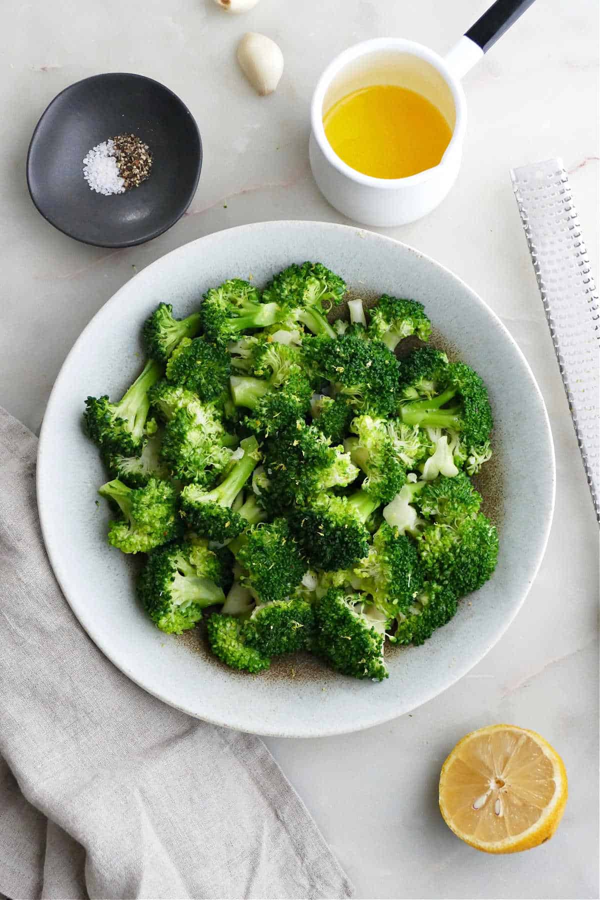 boiled broccoli in a serving bowl next to seasonings on a counter