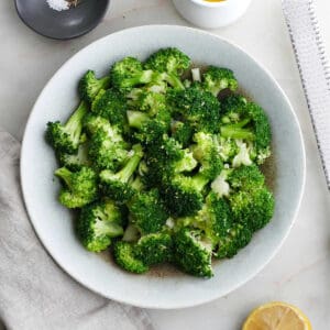 boiled broccoli in a serving bowl next to seasonings on a counter