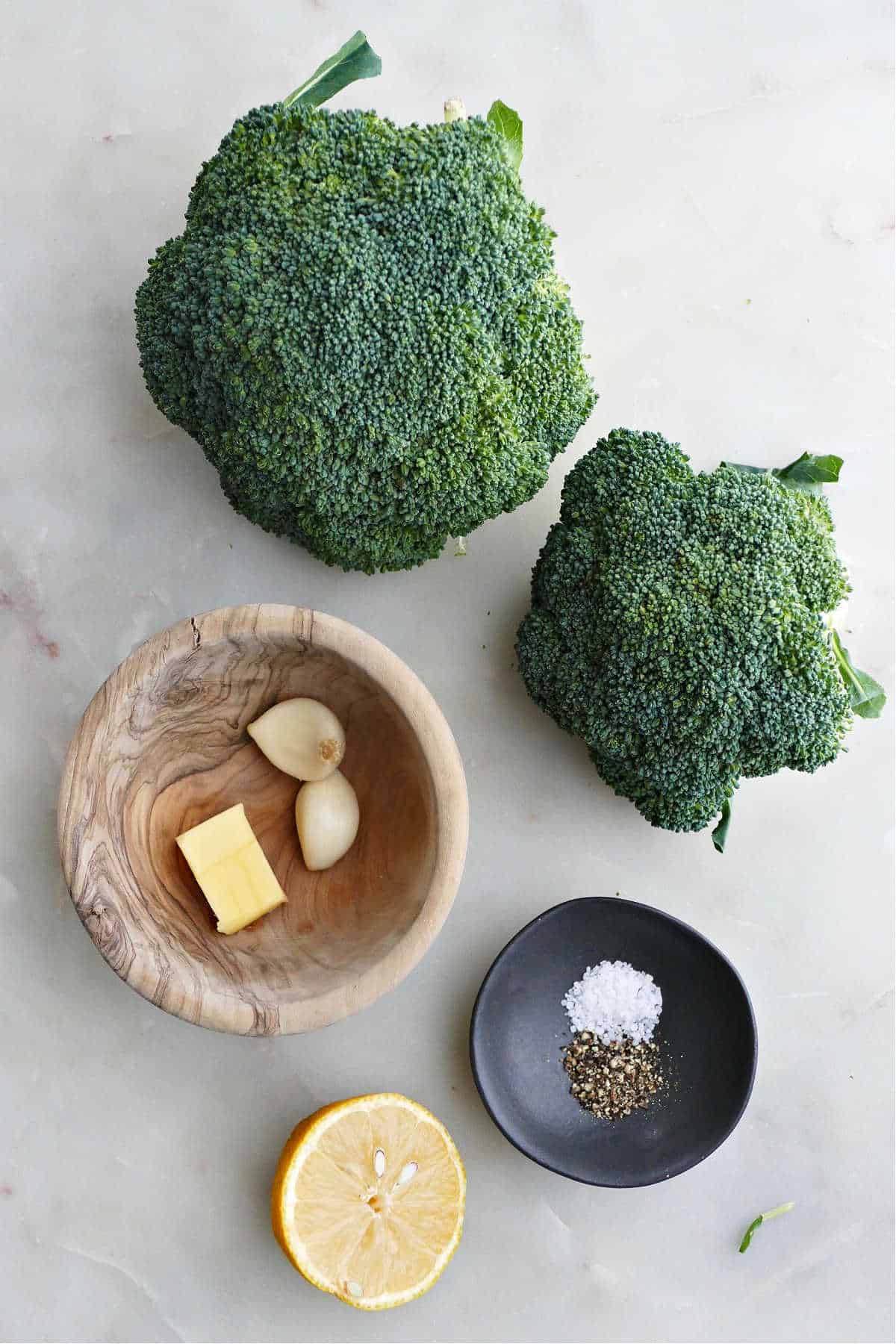 heads of broccoli, salt, pepper, garlic, butter, and lemon on a counter