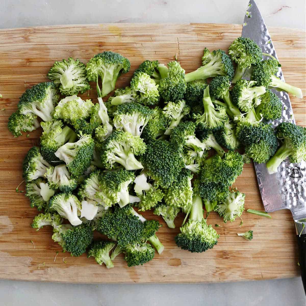broccoli cut into florets on a cutting board with knife