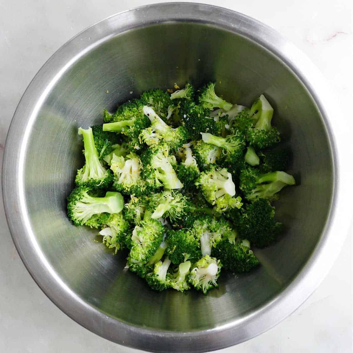 broccoli being mixed with seasonings in a bowl after being cooked