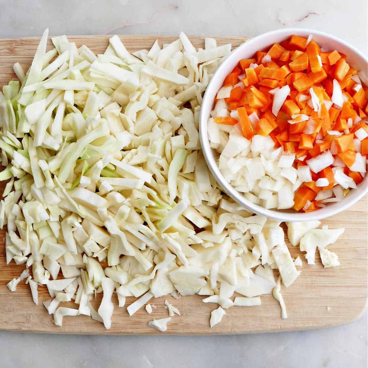 sliced cabbage on a cutting board next to bowl with onions and carrots