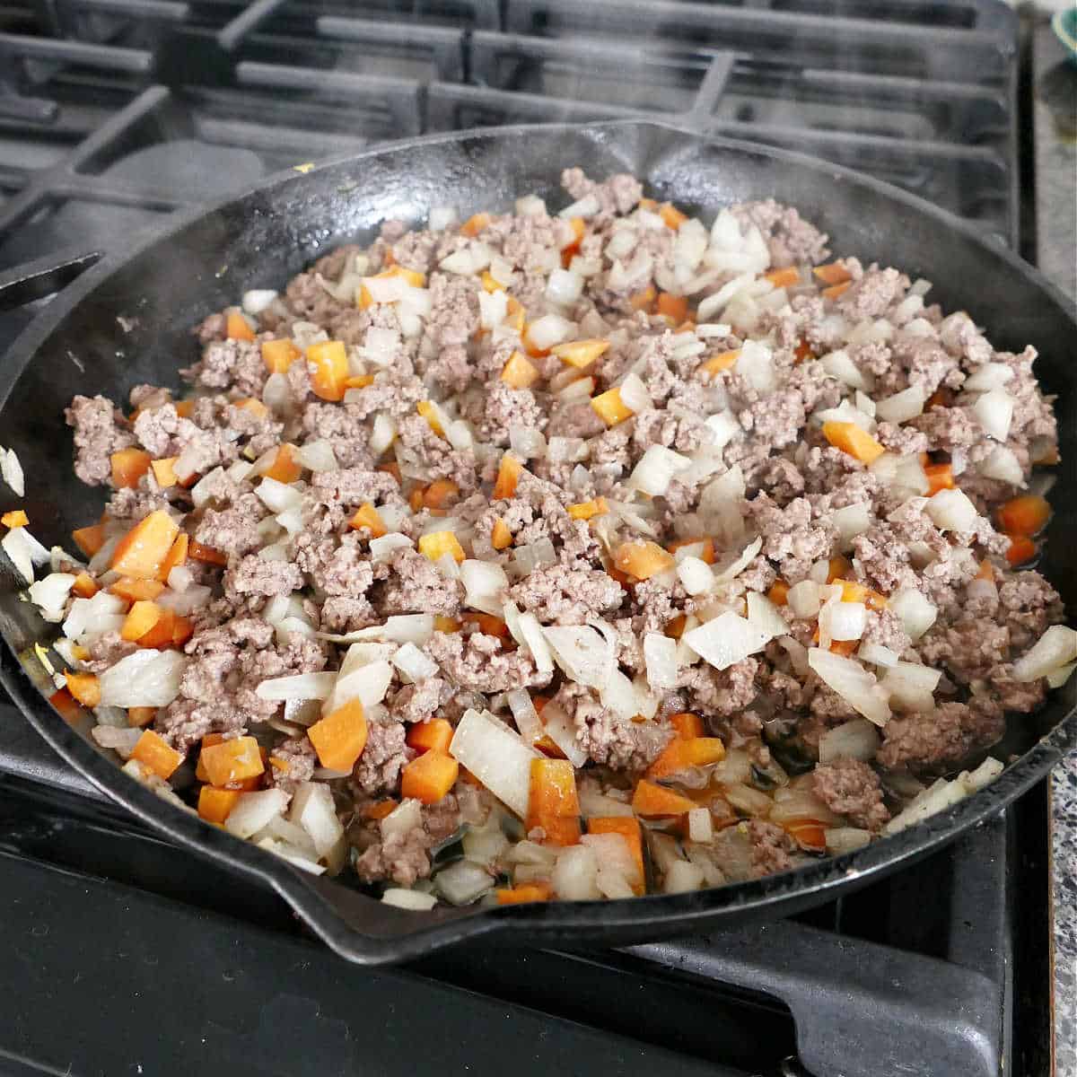 chopped vegetables and ground beef cooking in a cast iron skillet