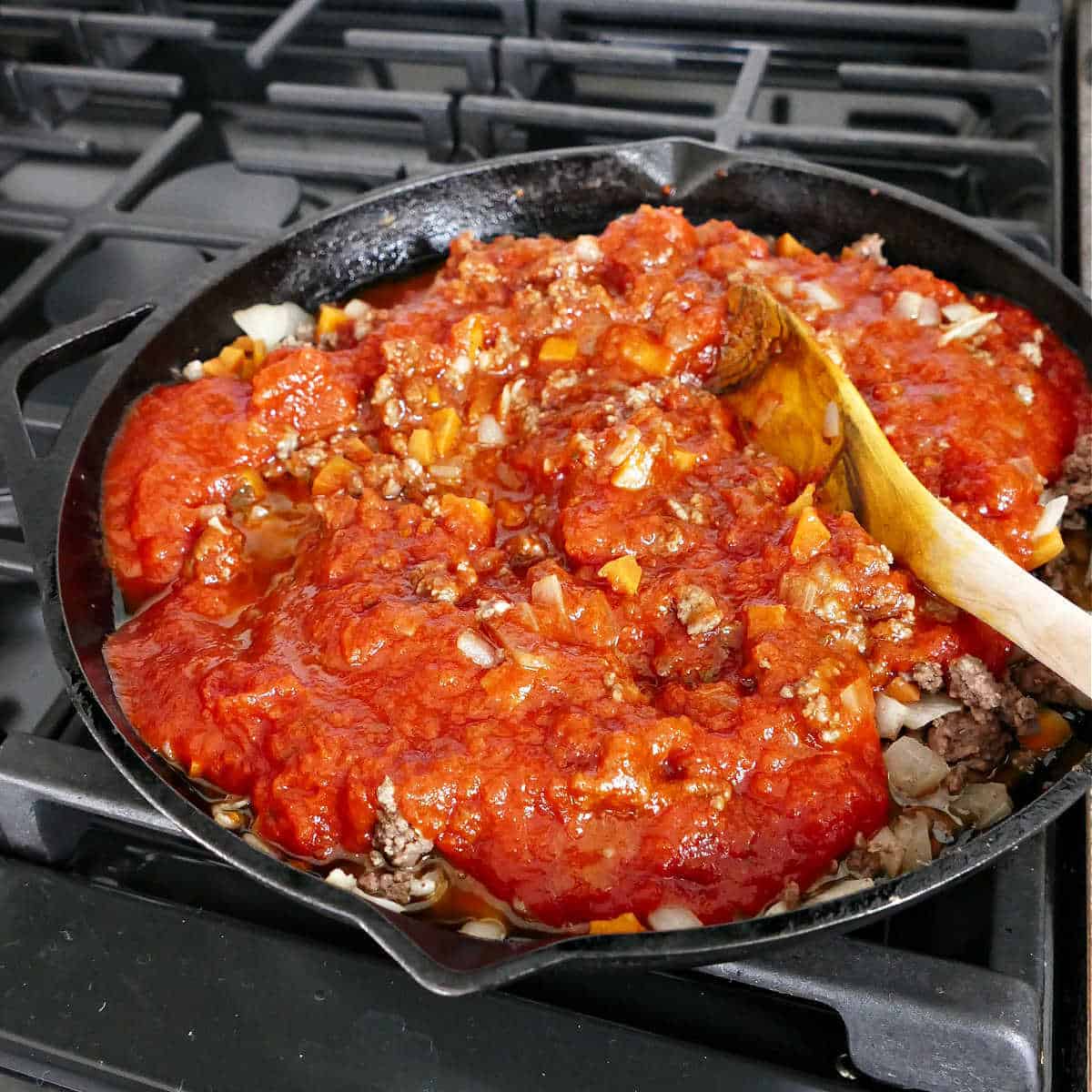 ground meat and vegetables cooking in tomato sauce in a cast iron skillet