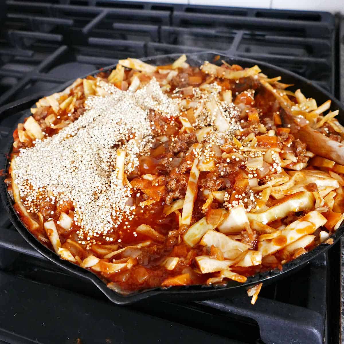 cabbage, beef, and vegetables with quinoa added cooking in a skillet