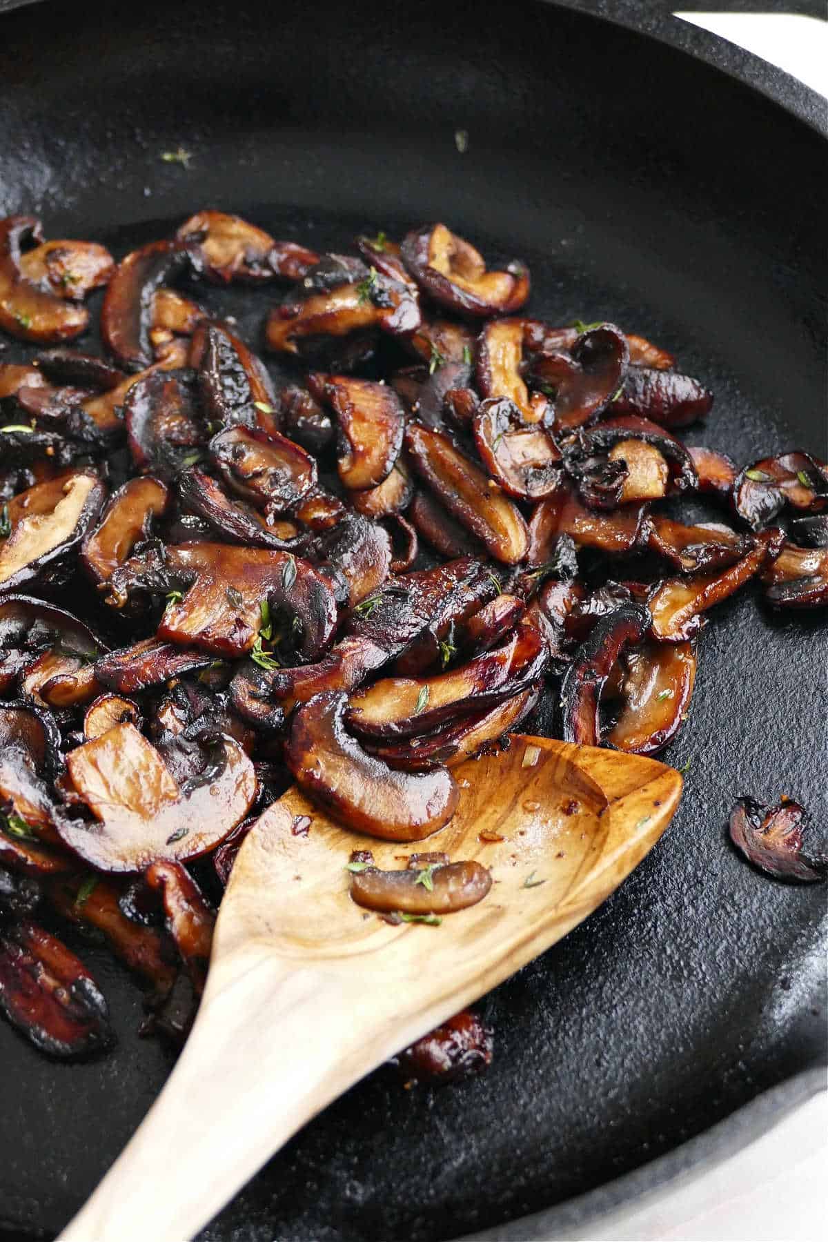 crispy mushrooms with thyme in a cast iron skillet with a wooden spoon