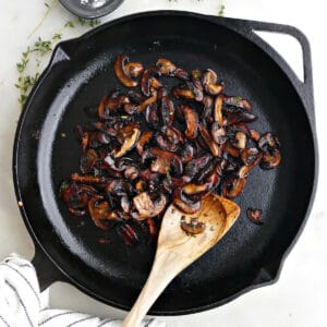 caramelized mushrooms in a cast iron skillet with a spoon on a counter