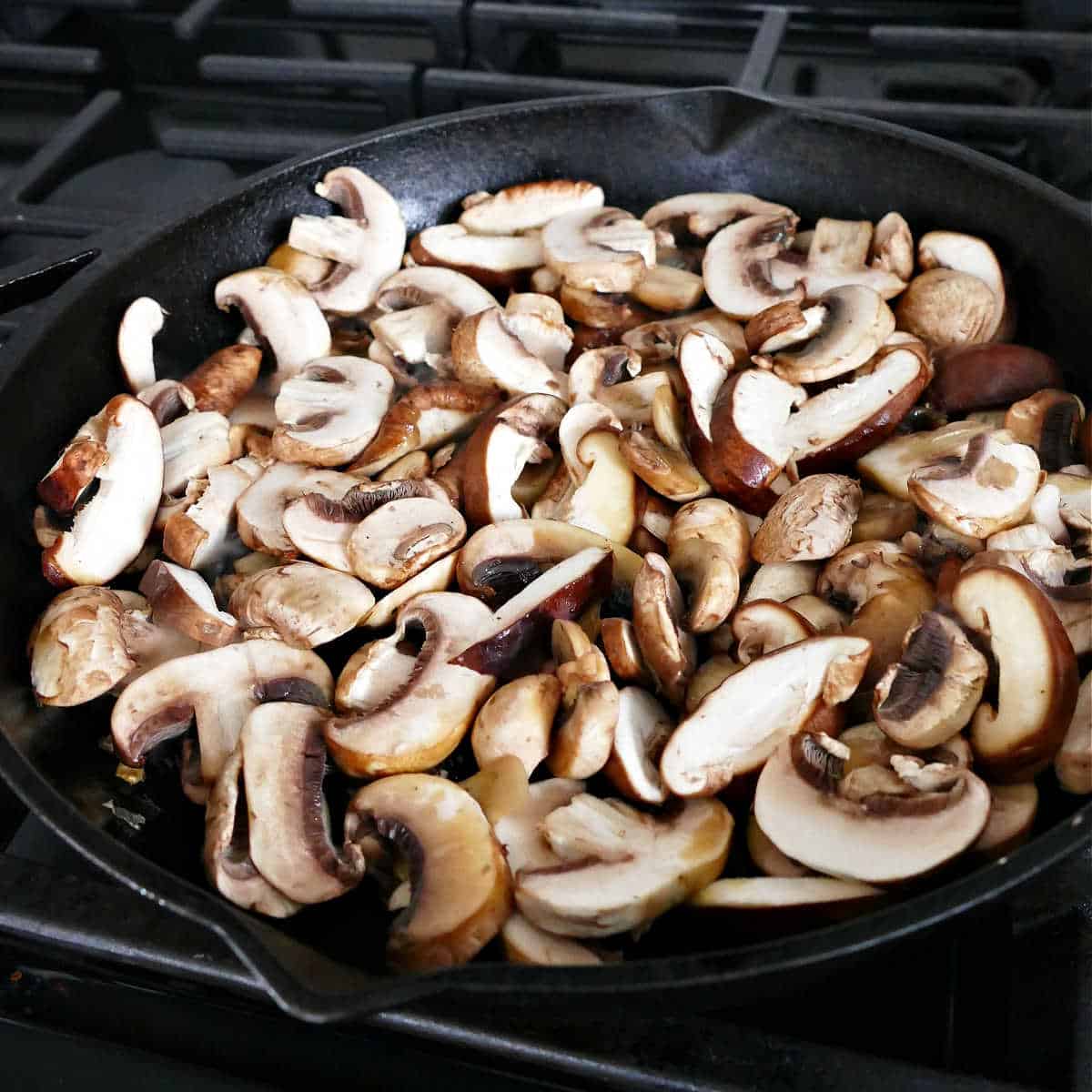 sliced mushrooms cooking in a cast iron skillet on a stove