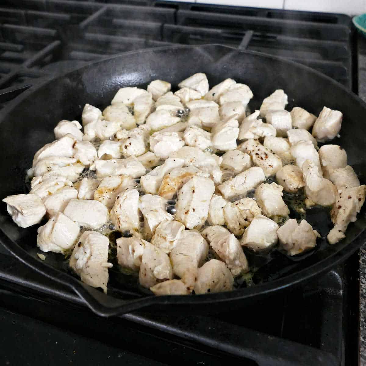 diced chicken cooking in a cast iron skillet on the stove