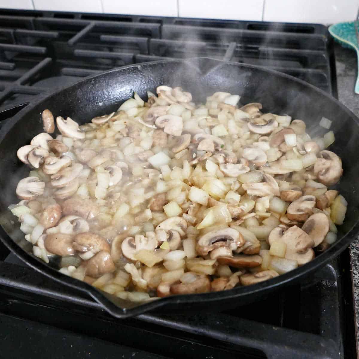 mushrooms and onions cooking in a cast iron skillet on a stove