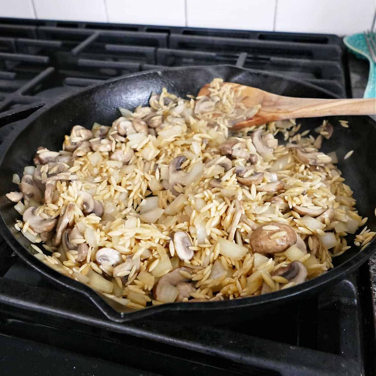 mushrooms, onion, and orzo cooking in a cast iron skillet