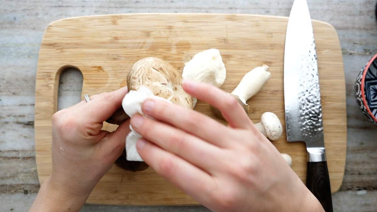 woman wiping a mushroom with a damp towel over a cutting board