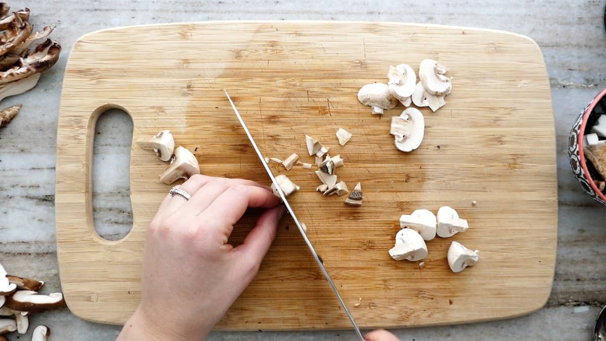 woman chopping a button mushroom into pieces on a cutting board